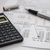 A calculator and pen laying on billing and acocunting documents